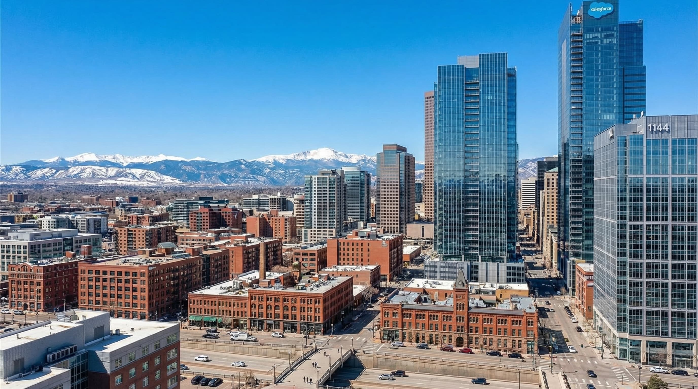 Denver Colorado skyline with Rocky Mountain backdrop, historic brick buildings in LoDo, and clear blue Colorado sky